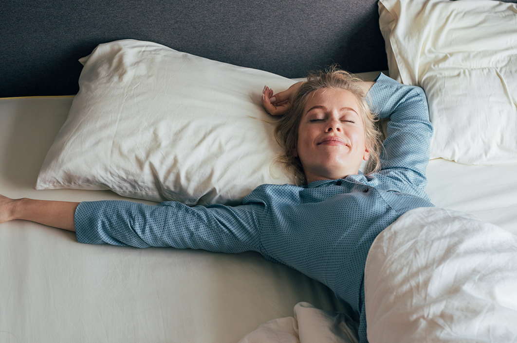 Une femme est allongée dans un lit avec un bras écarté et elle sourit.